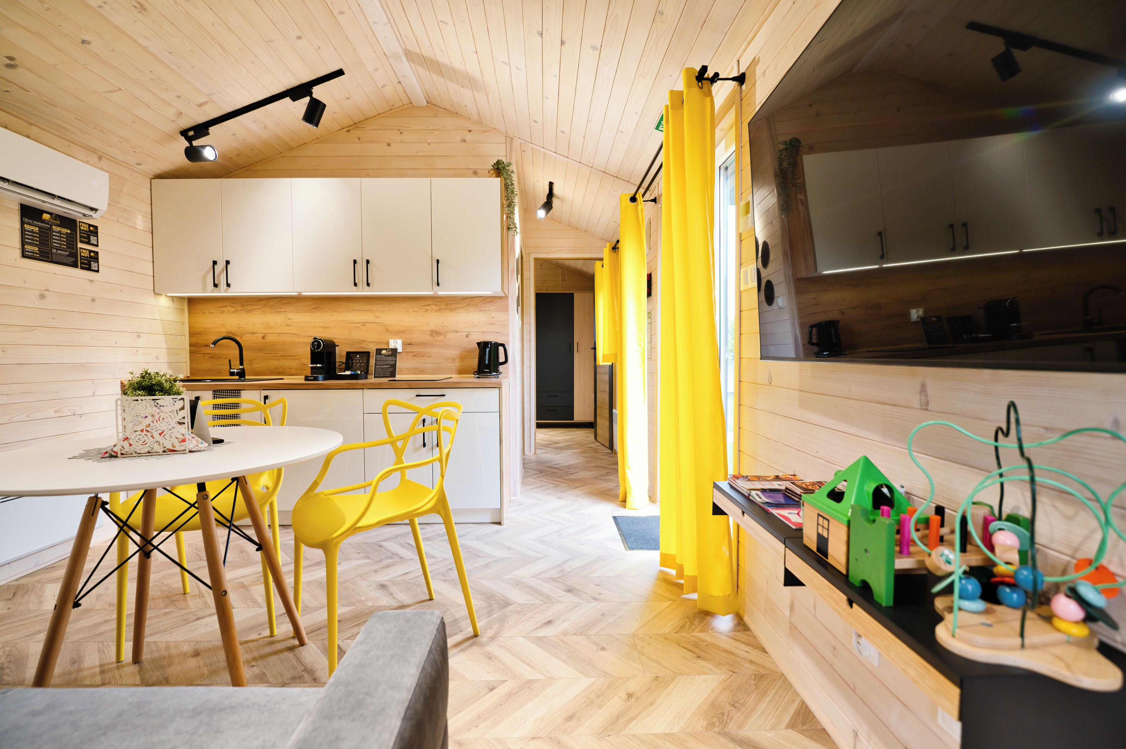 A modern kitchen with white cabinets, a dining area with yellow chairs, and a play area with toys.