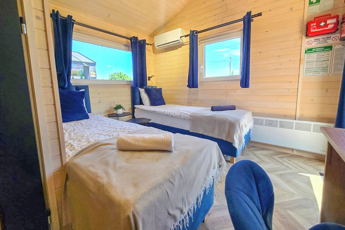A cabin with two beds, a small table, and a chair. There are curtains, an air conditioning unit, and a window with a view.