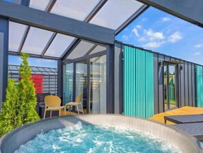 Ein moderner Außenbereich mit Whirlpool, Glastüren, einer Sitzecke und Blick auf den Himmel.
