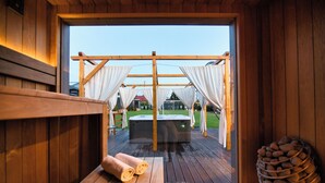 Una cabaña de madera con jacuzzi, terraza de madera y vista a un espacio cubierto de césped.
