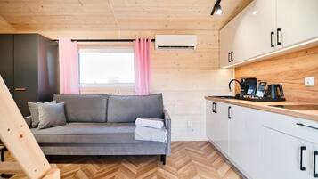 A compact living space with a sofa, kitchenette, and wooden flooring.
