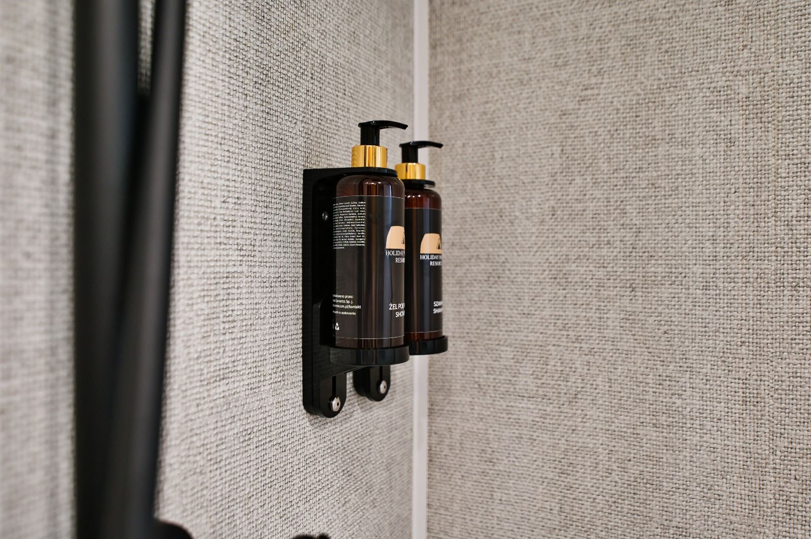 Dispensador de pared con dos botellas de jabón líquido y un dosificador.