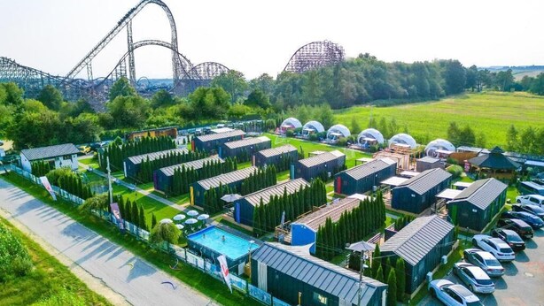 Un gran complejo industrial con varios edificios, una piscina y una montaña rusa al fondo.