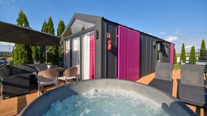 Un área moderna de hidromasaje al aire libre con asientos y un pequeño edificio con cortinas rosadas.