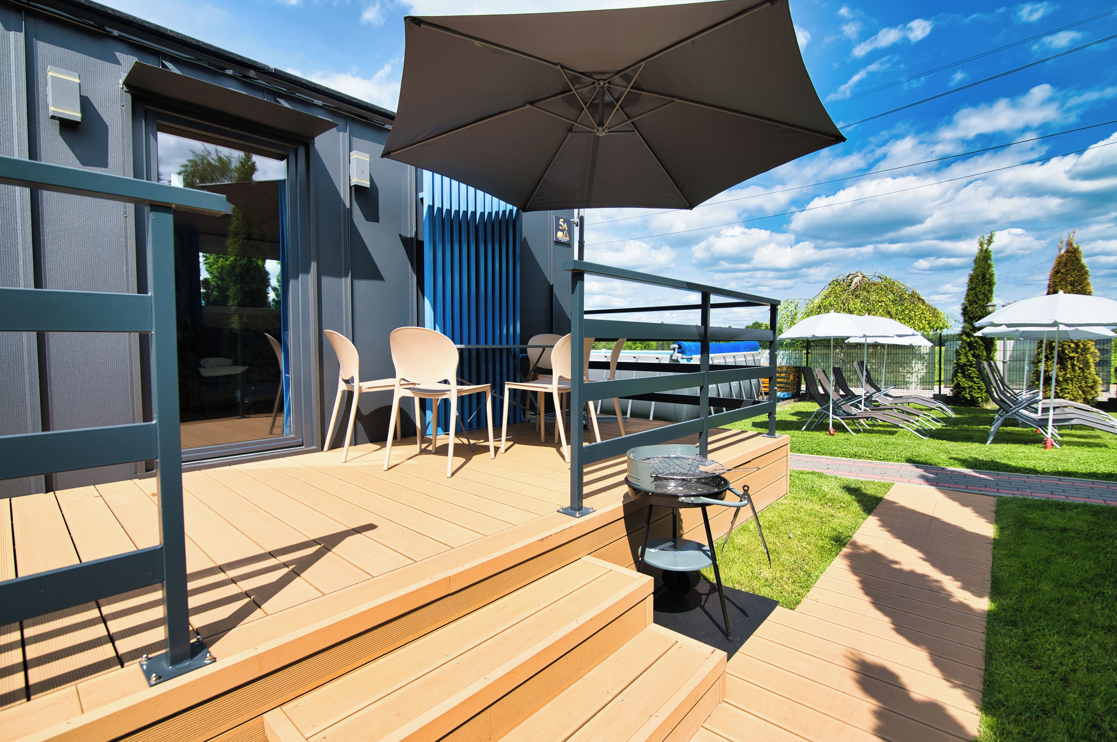A wooden deck with outdoor seating, a grill, and umbrellas.