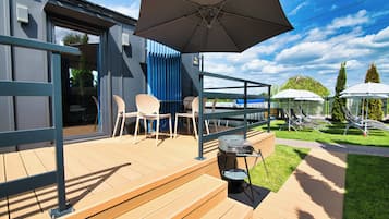 A wooden deck with outdoor seating, a grill, and umbrellas.