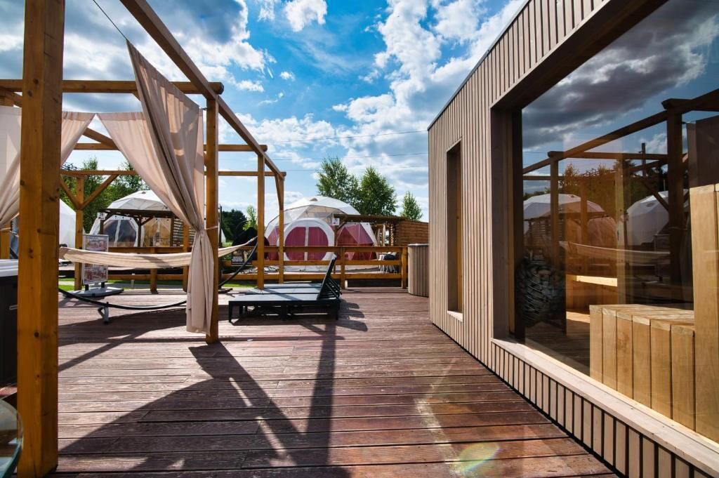 A wooden deck with a hammock, a covered seating area, and a glass enclosure.