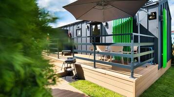A modern outdoor seating area with a metal railing, a large umbrella, and a grill.