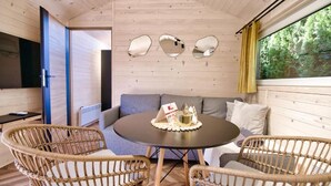 Una habitación acogedora con una mesa redonda, sillas de mimbre, un sofá y un gran ventanal con vistas a árboles.