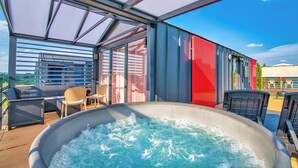 Un área de piscina en la azotea con un jacuzzi, mobiliario exterior y vistas del paisaje circundante.
