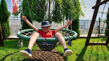 Un enfant sur une balançoire dans un parc, avec une clôture en treillis et des arbres en arrière-plan.