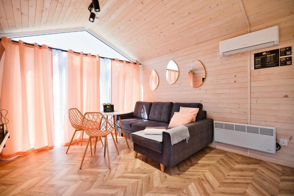A cozy room with a sofa, a table, and chairs. There is a window with curtains, a mirror on the wall, and an air conditioning unit.