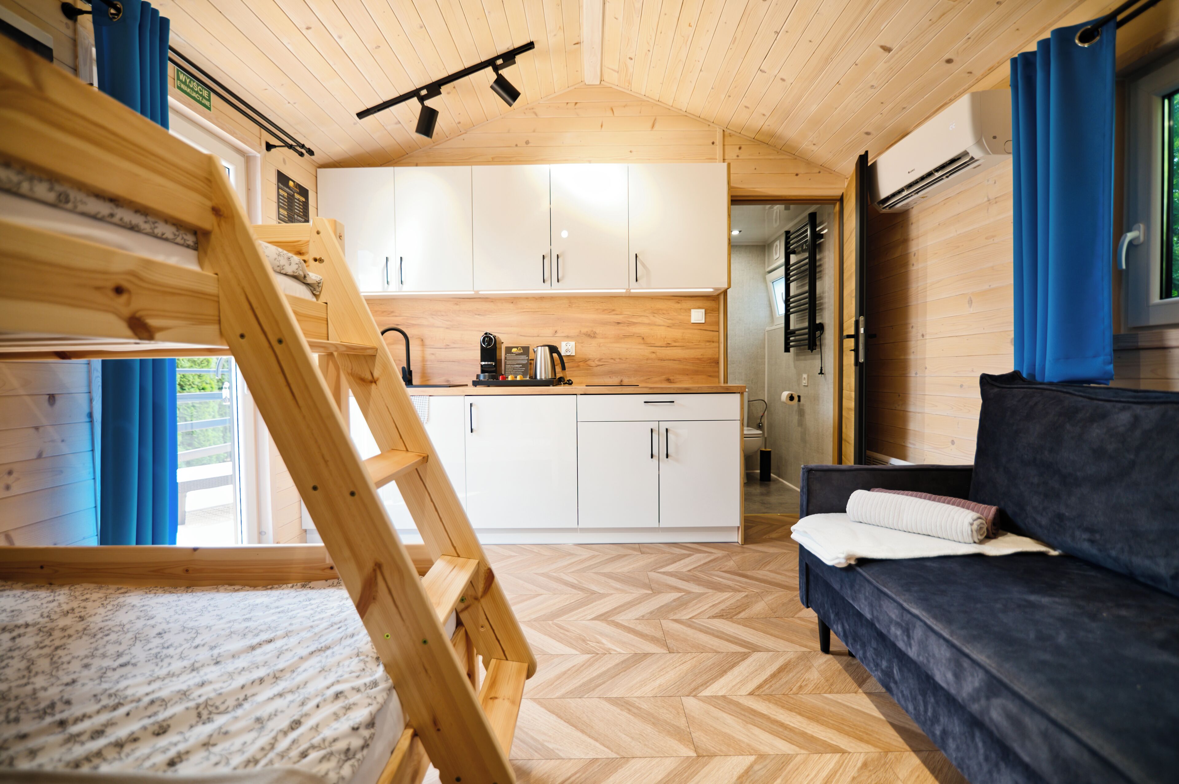 A compact room with a bunk bed, kitchenette, and a sofa.