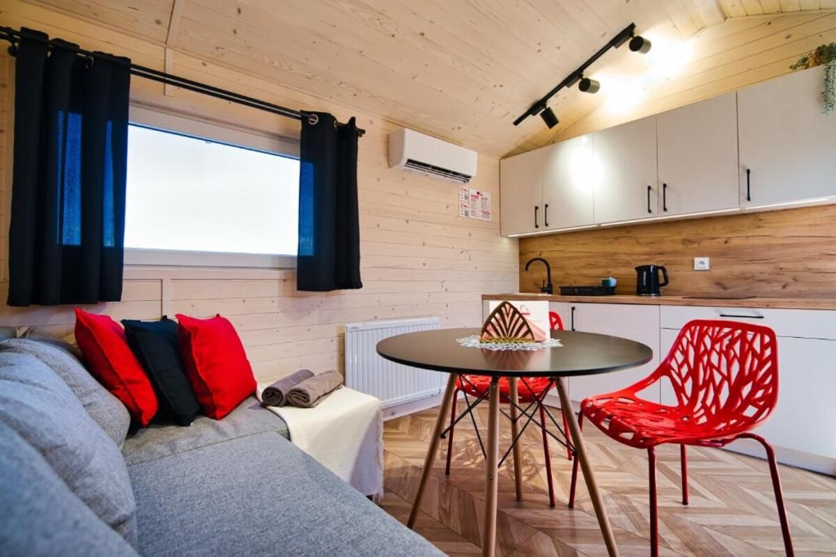 Un espacio habitable compacto con kitchenette, zona de comedor con mesa y sillas, y sofá con cojines.