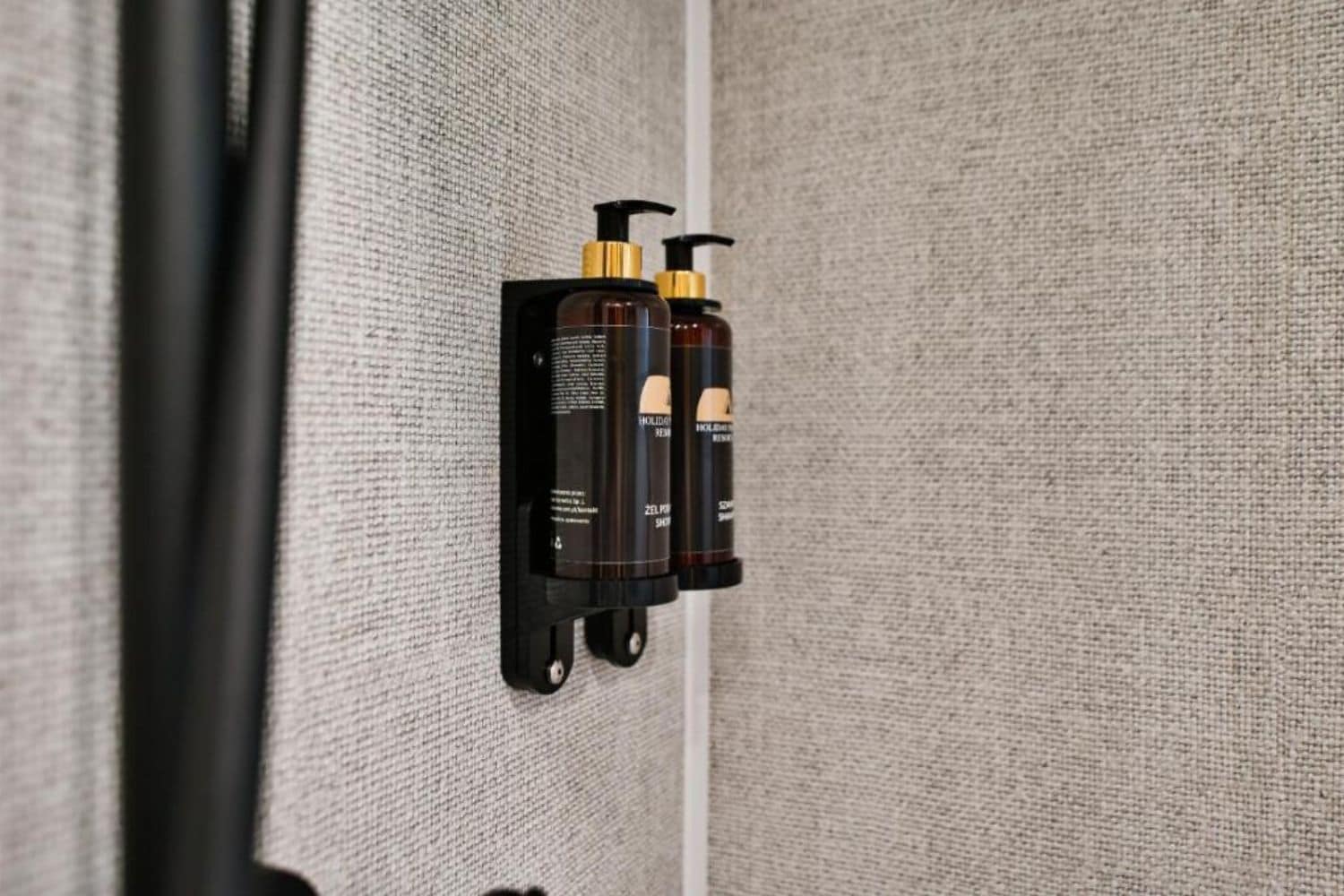 Dispensador de pared con dos botellas, probablemente de artículos de aseo, en una habitación de hotel.