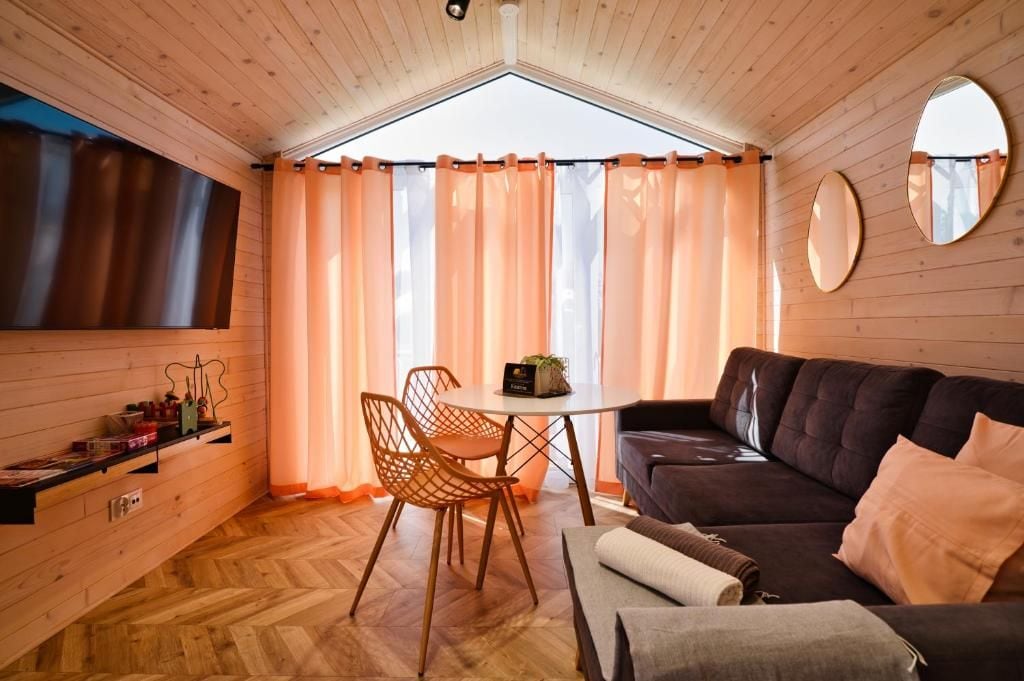Une pièce chaleureuse avec un plafond en bois, un canapé sombre, une petite table et une fenêtre avec des rideaux.