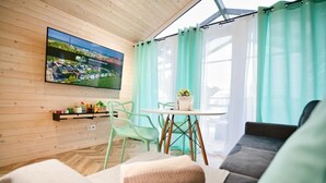Una sala de estar moderna con techo de madera, un televisor de pantalla plana, una mesa redonda con planta en maceta y sillas verdes.
