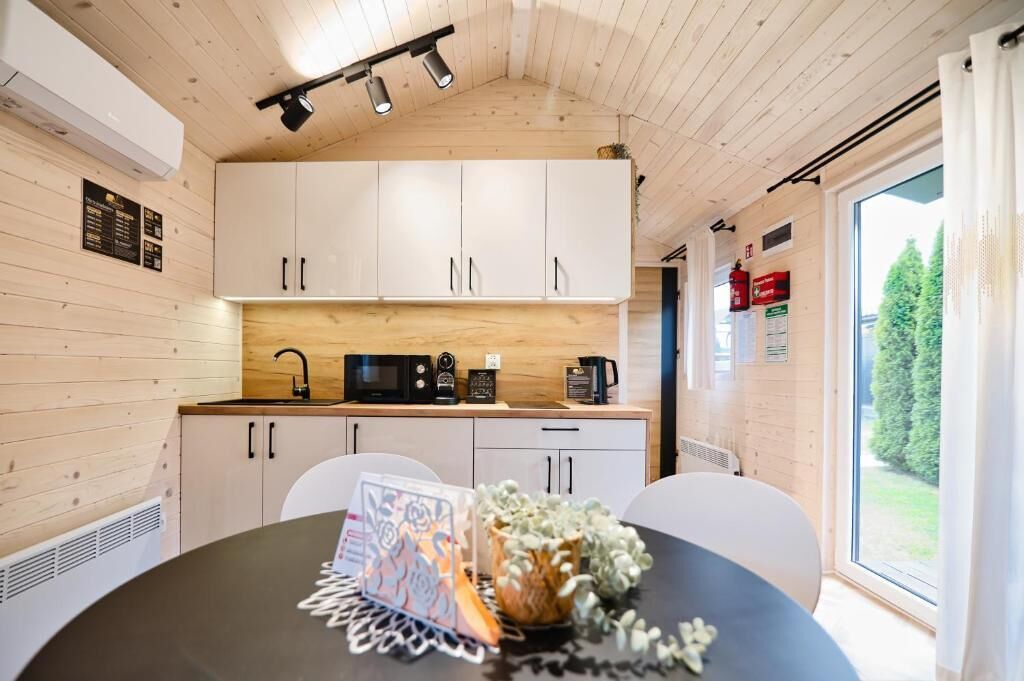 A compact kitchen with white cabinets, a microwave, and a coffee maker. There is a dining table with a placemat and a vase with flowers.