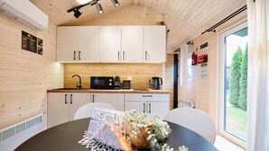 Una cocina compacta con gabinetes blancos, microondas y cafetera. Hay una mesa de comedor con un mantel individual y un florero con flores.