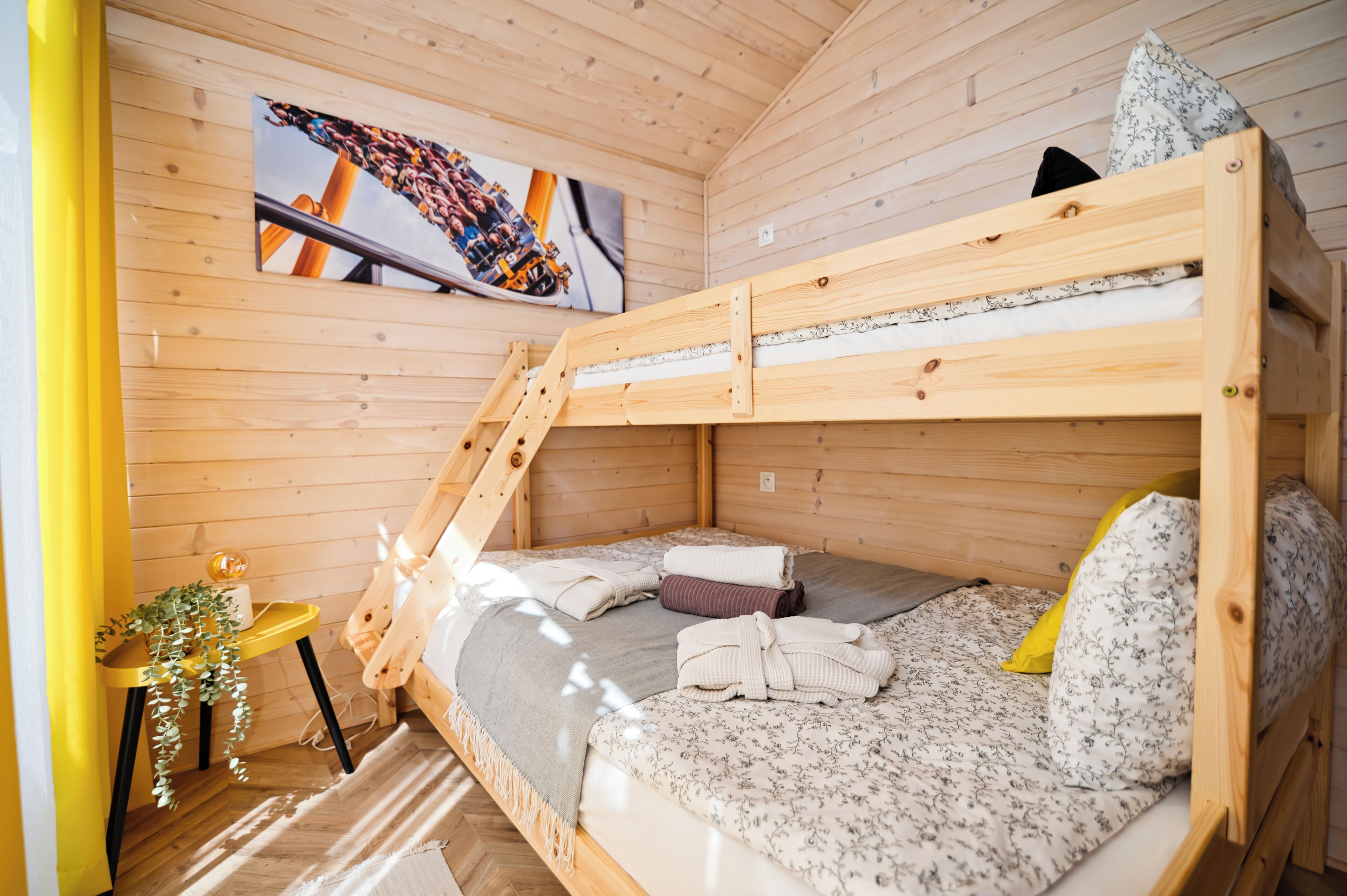 A bunk bed room with wooden walls, a small table with a plant, and a painting on the wall.