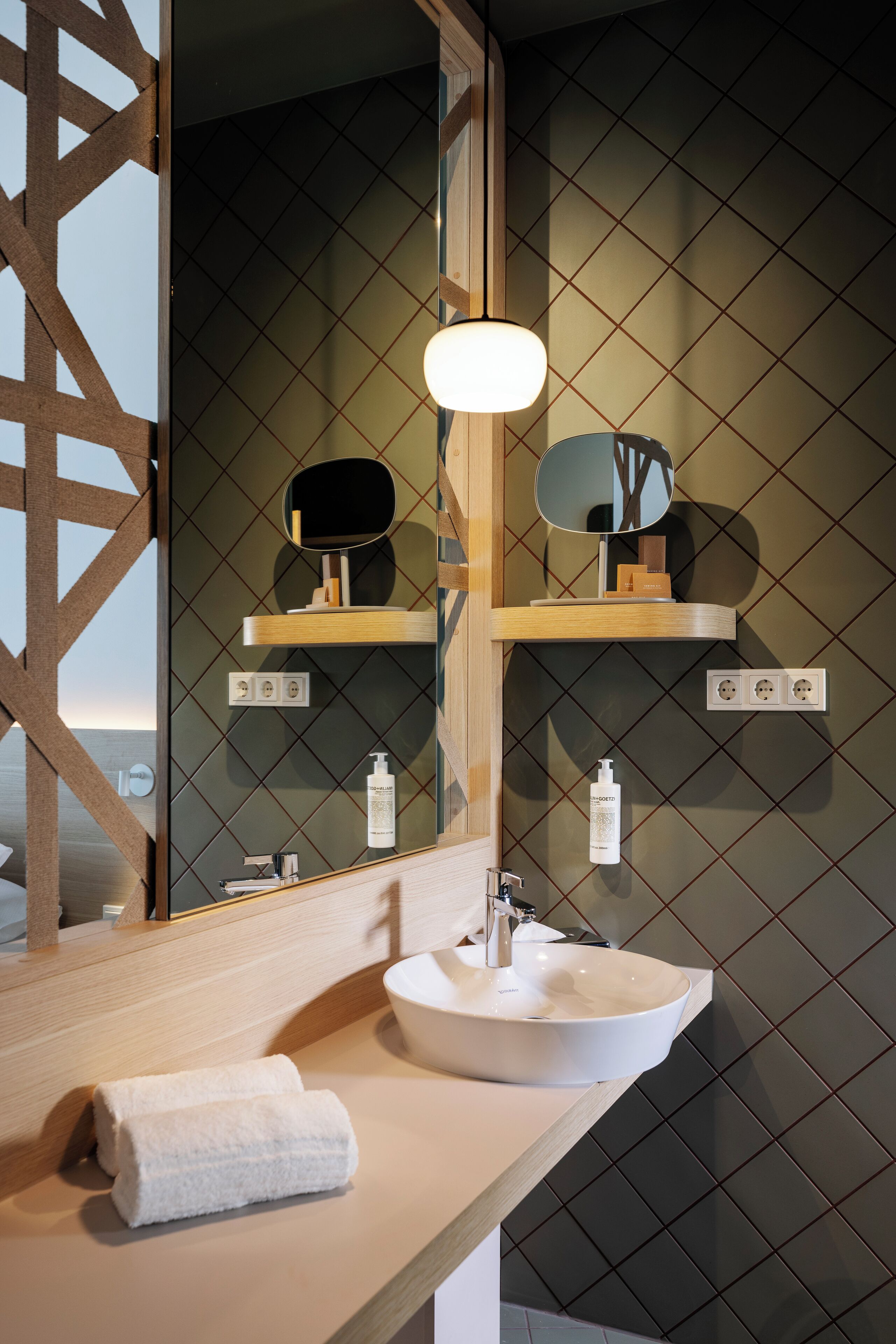 Ein modernes Badezimmer mit einem großen Spiegel, einem weißen Waschbecken und einem Handtuch auf der Ablagefläche.