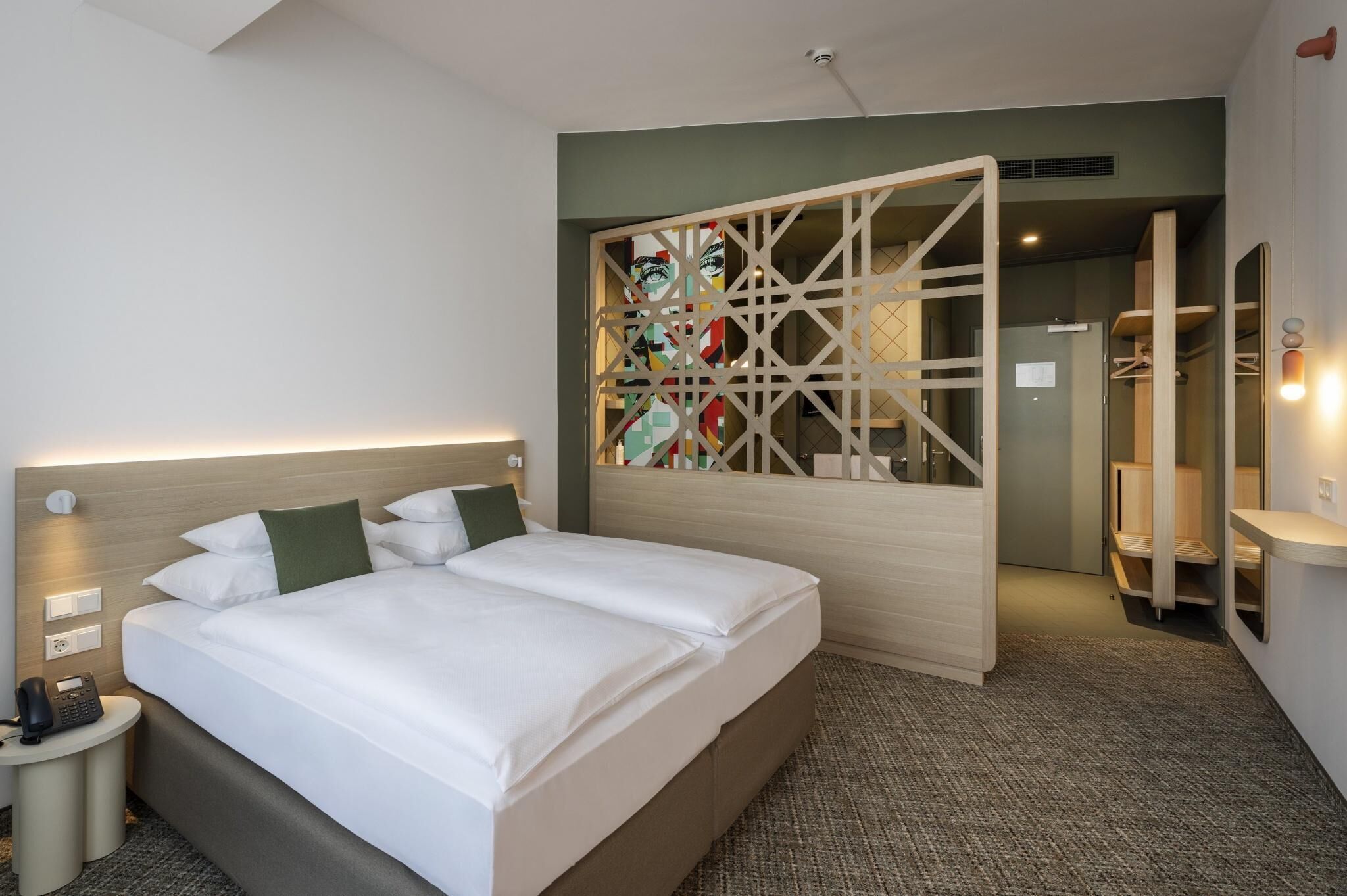 A hotel room with a large bed, a bedside table with a phone, and a wall-mounted light.