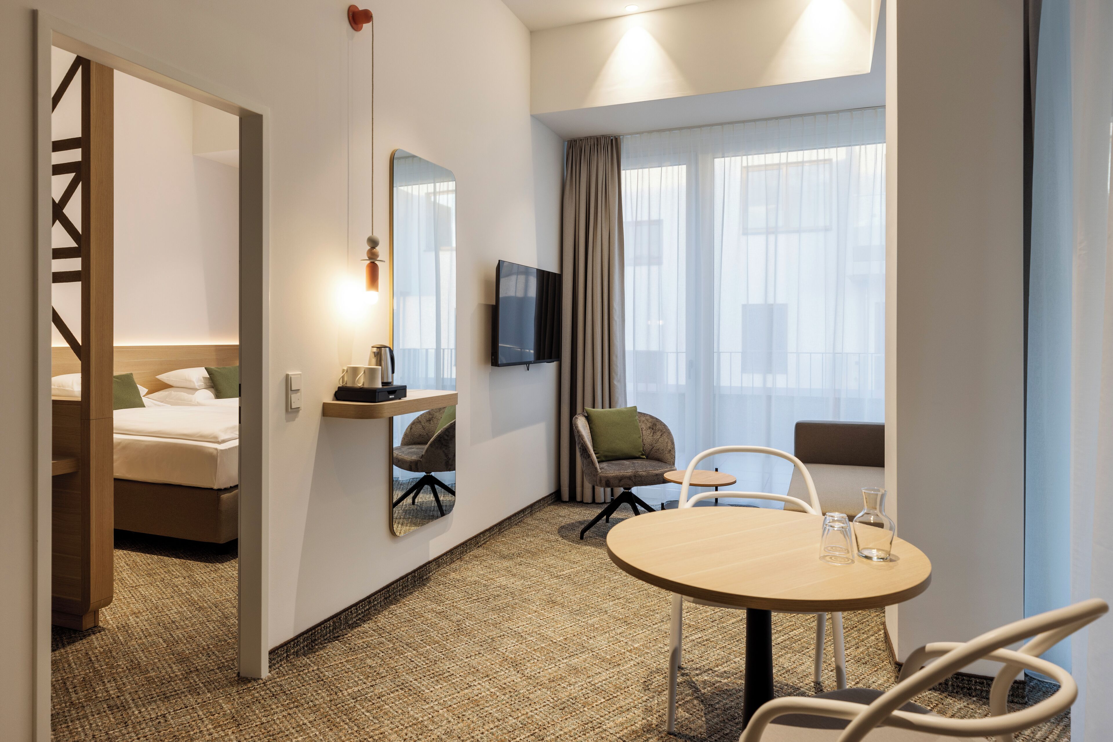 Ein Hotelzimmer mit Bett, Schreibtisch, Stuhl, rundem Tisch, Fernseher und einem Fenster mit Vorhängen.