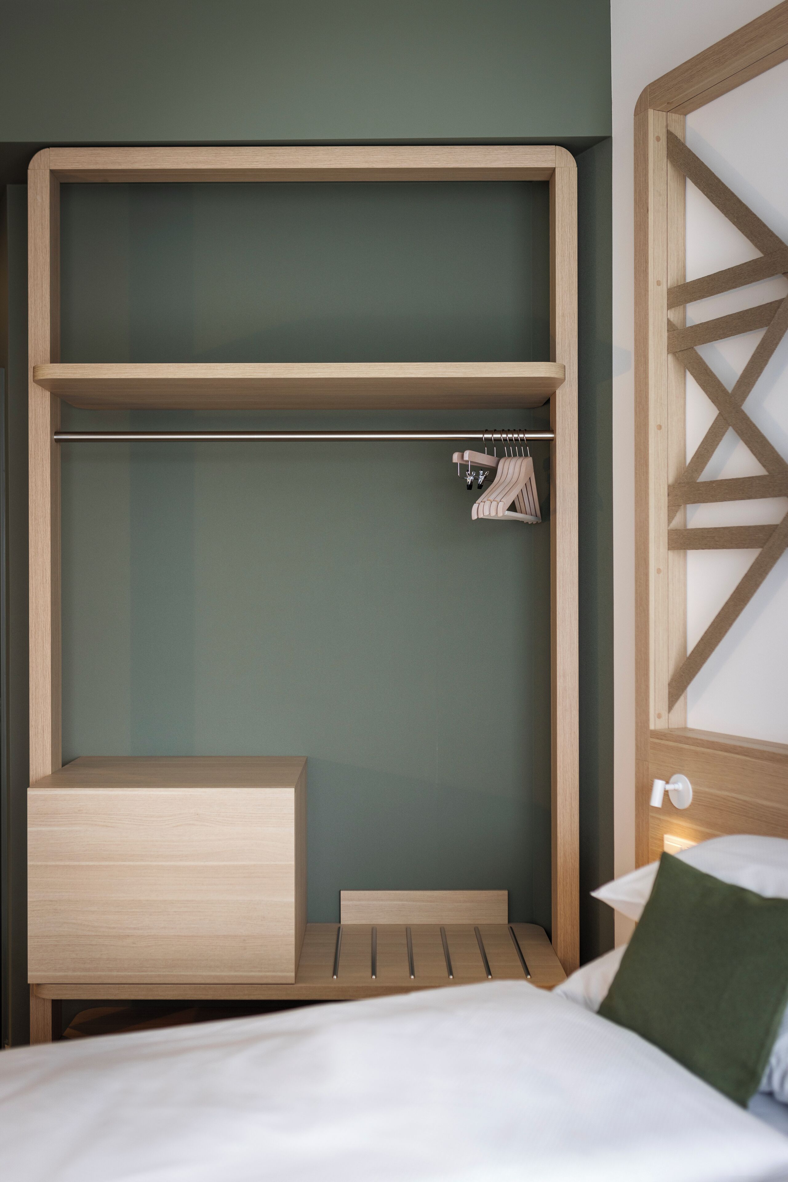 Una habitación moderna con un armario empotrado de madera, una mesita de noche y una cama con un cojín verde.