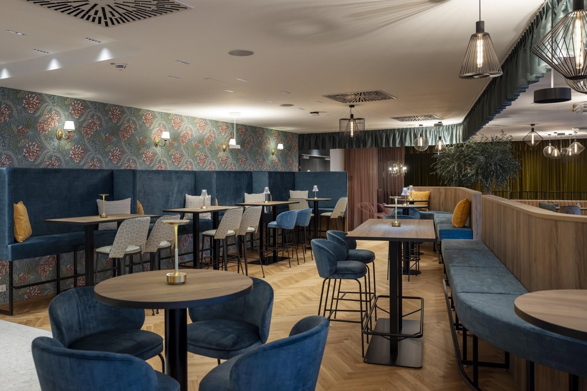 A modern restaurant with round tables, blue upholstered seating, and patterned wallpaper.