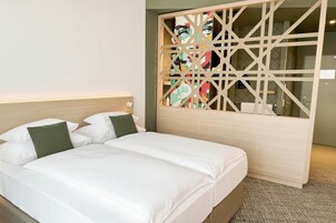 Quarto de hotel com cama, cabeceira e divisória decorativa com obras de arte.