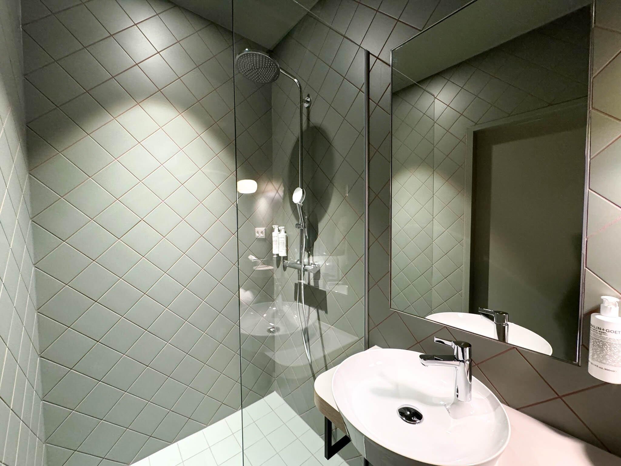 A modern bathroom with a glass-enclosed shower, a white sink, and a large mirror.