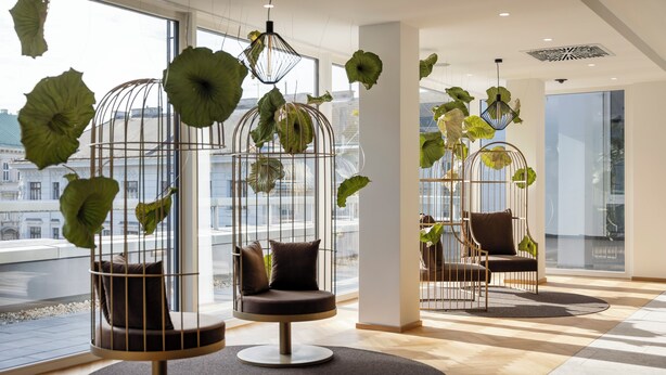 A modern interior with three hanging chairs, each with a cushion and a metal cage. - ARCOTEL AQ Wien (Vienna)