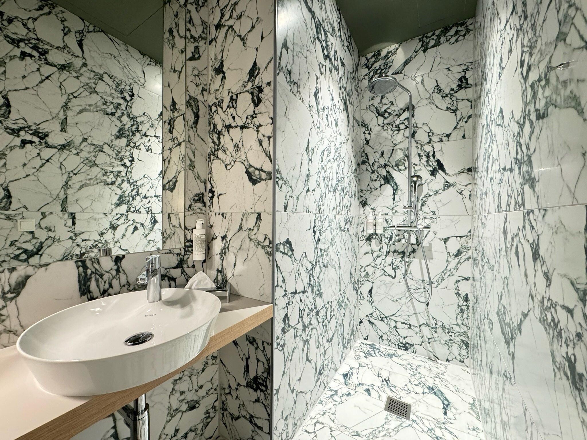 Un baño con lavamanos de mármol blanco, ducha de mano y pared de mármol.