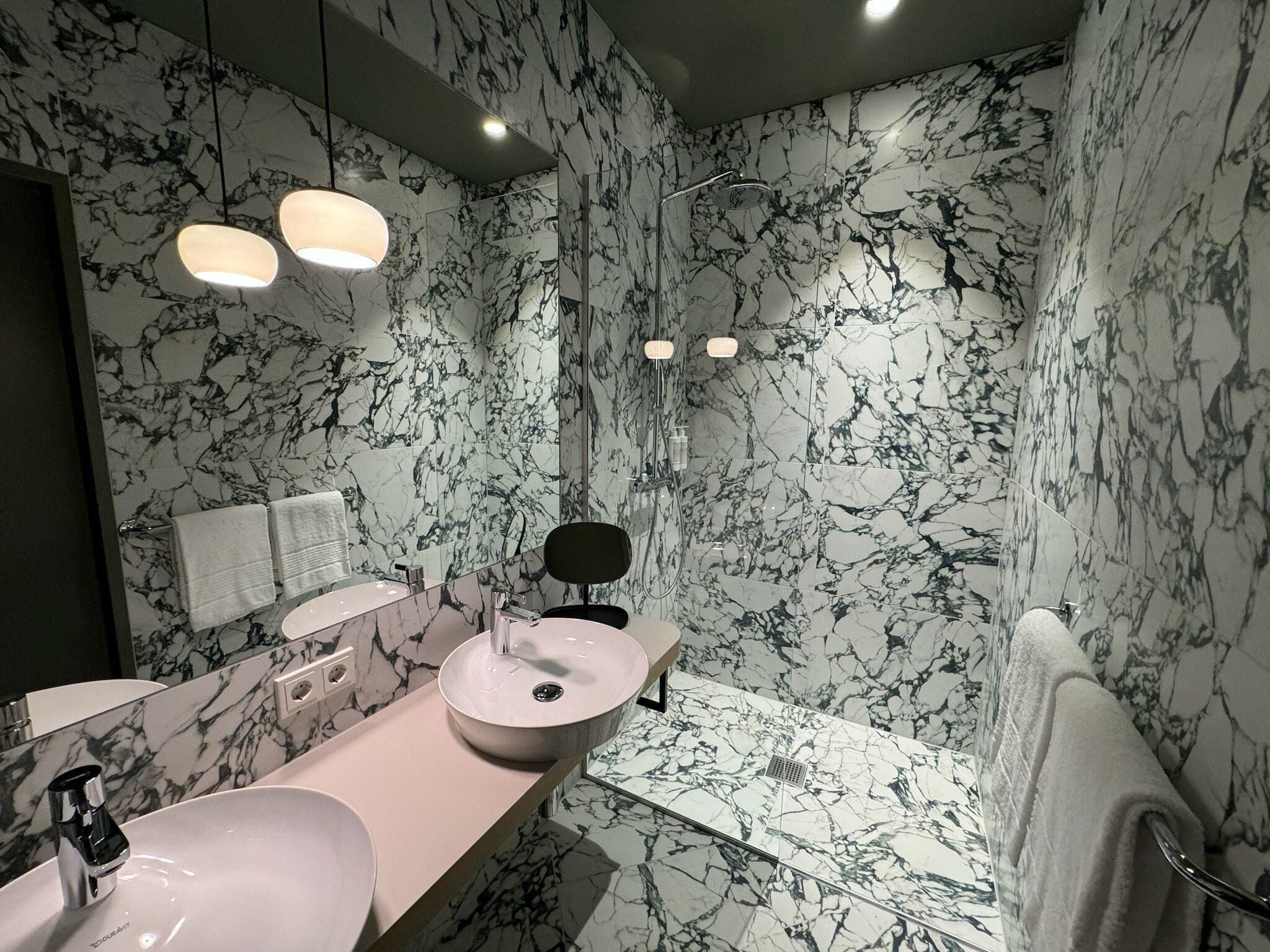 Une salle de bain moderne avec des murs en marbre, un meuble-lavabo doté de deux vasques, un miroir et un espace douche.
