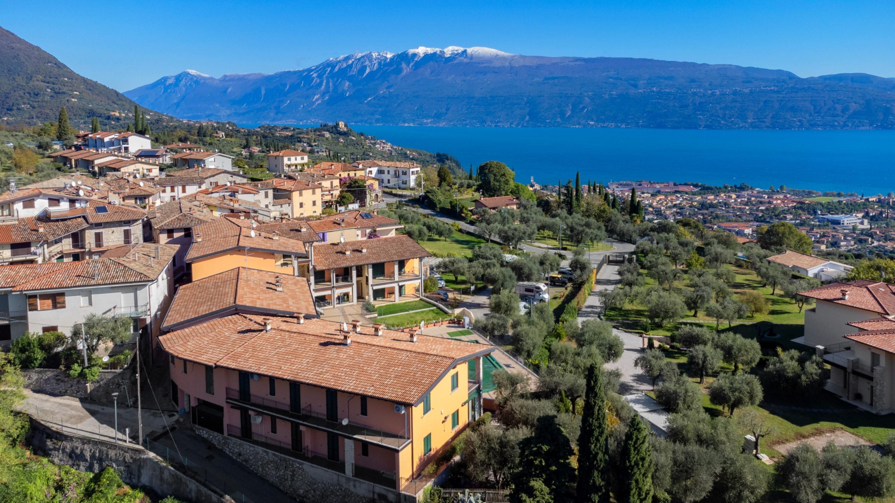 Uma vila costeira com edifícios de telhados de terracota, vista clara do mar e uma cordilheira ao fundo.