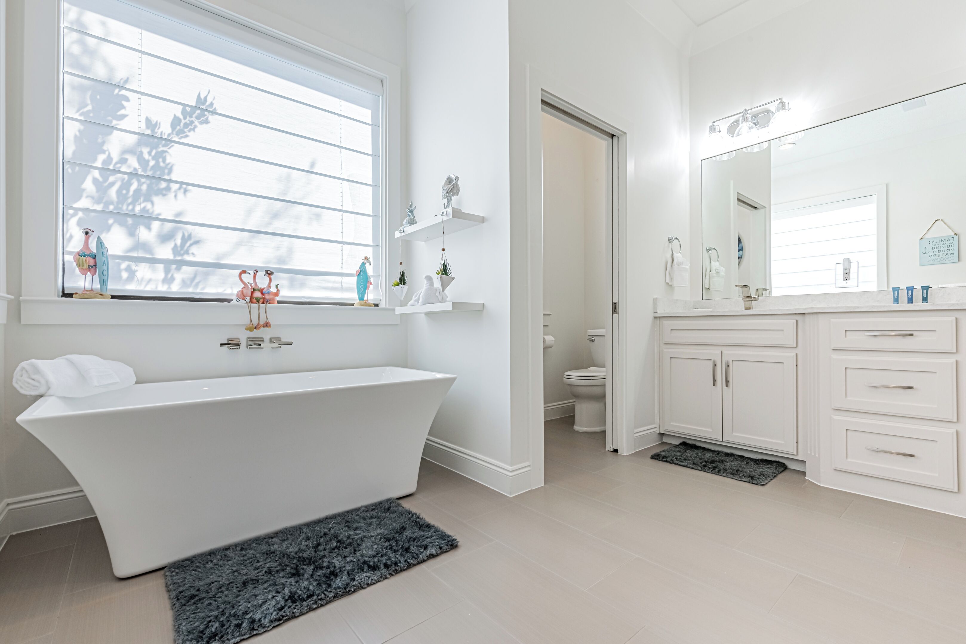 Une salle de bain moderne avec une baignoire sur pieds, un grand miroir et des toilettes visibles à travers une porte ouverte.