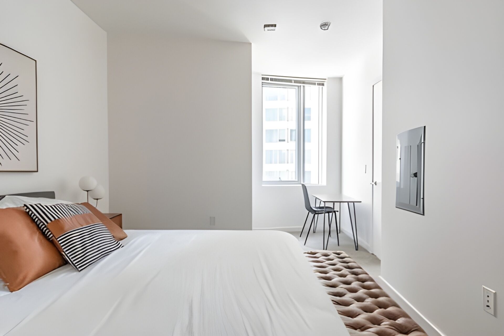 A modern bedroom with a bed, a chair, a table, and a window with a city view.