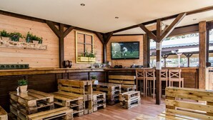Un interior rústico de madera con palés de madera como asientos, un televisor montado en la pared y una barra de bar de madera con estantes arriba.