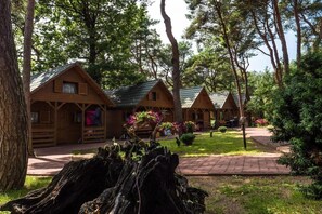 Uma fileira de cabanas de madeira com telhados inclinados, cercada por árvores e um espaço gramado.