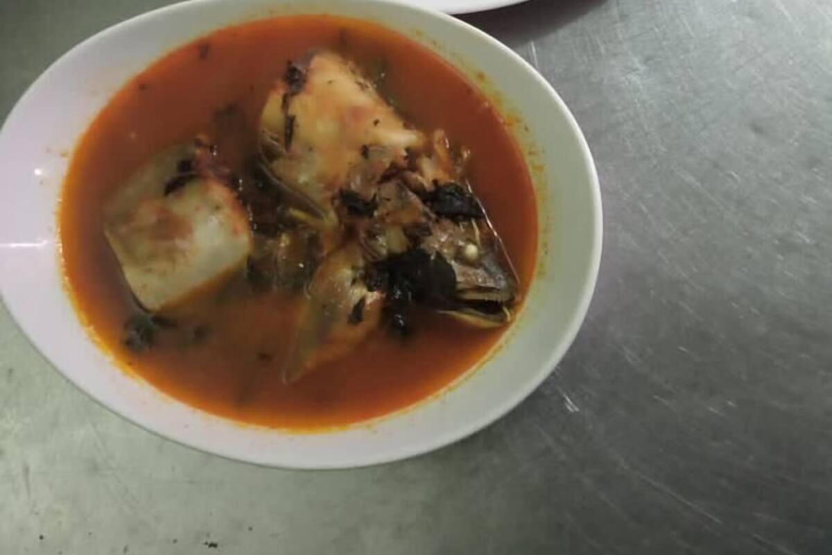 Eine weißer Reis Teller, garniert mit grünen Kräutern, und eine Schale Fischsuppe mit Fischstückchen und Gemüse in roter Sauce.