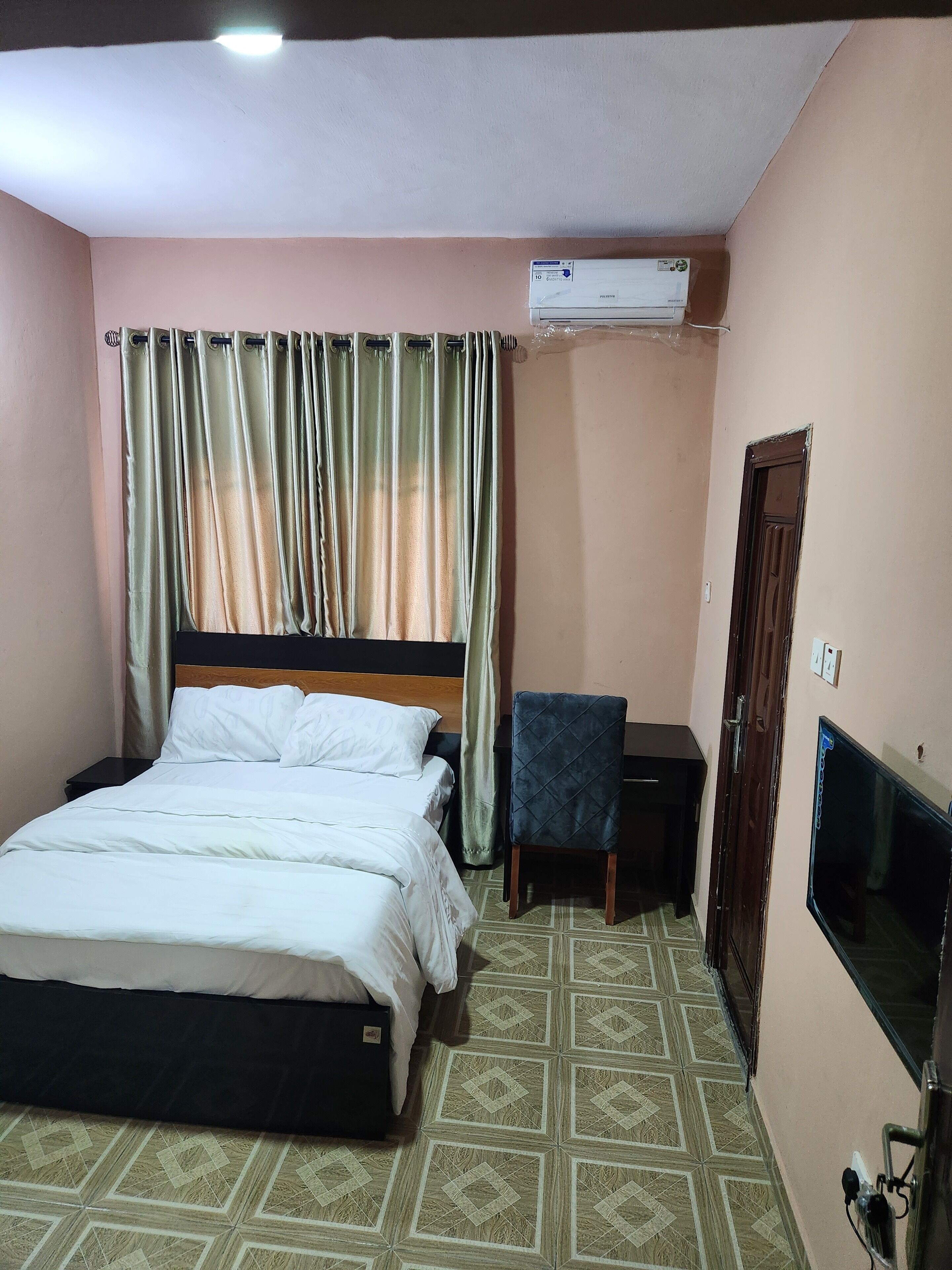 Una habitación de hotel con cama, escritorio, silla, aire acondicionado y televisión.