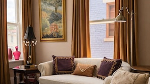 Een woonkamer met een bank, een bijzettafeltje, een lamp en een schilderij aan de muur.