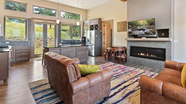 A spacious living area with a fireplace, a kitchen with large windows, and a dining area.