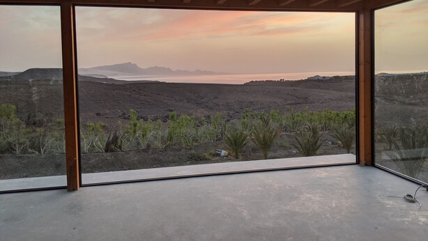 A room with large windows offering a view of a desert landscape with mountains and a body of water during sunset. - Casa Julie, Ferien in Absoluter Ruhe (La Pared)