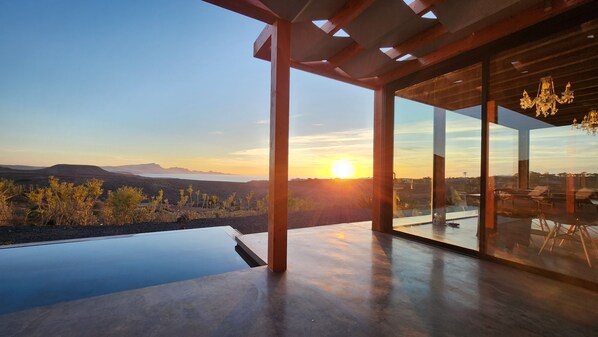 A modern outdoor space with a glass enclosure, a concrete floor, and a view of a sunset over a landscape.