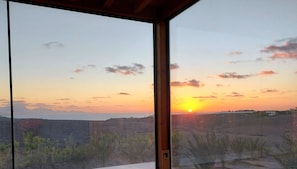 Vista al atardecer desde una habitación con ventanas amplias que dan a un paisaje montañoso.