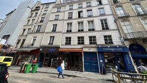 Un edificio a più piani con un negozio con la scritta "Les Caves du Louvre" e una porta blu con un segnale di divieto di parcheggio.