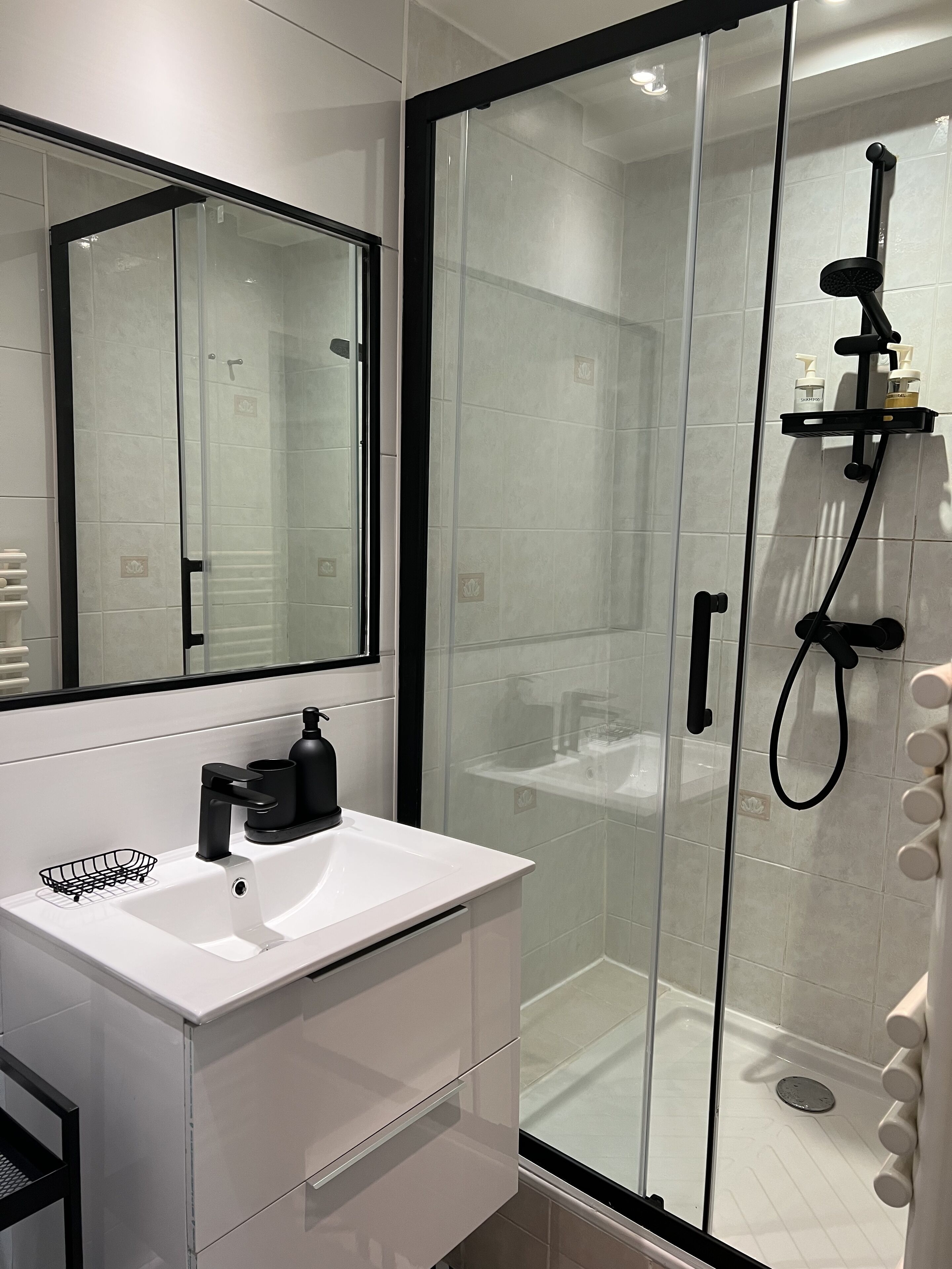 Un baño moderno con ducha de vidrio, tocador blanco con lavabo y un espejo grande.