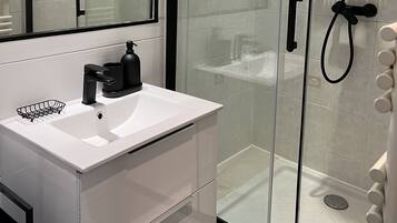Un baño moderno con ducha de vidrio, tocador blanco con lavabo y un espejo grande.