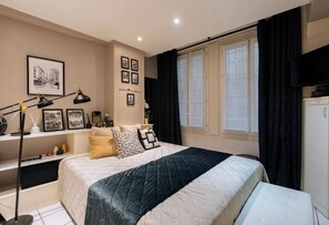 A bedroom with a bed, bedside tables, a desk, a lamp, and a window with curtains. - Louvre-Rivoli 1 bedroom apartment (Paris)